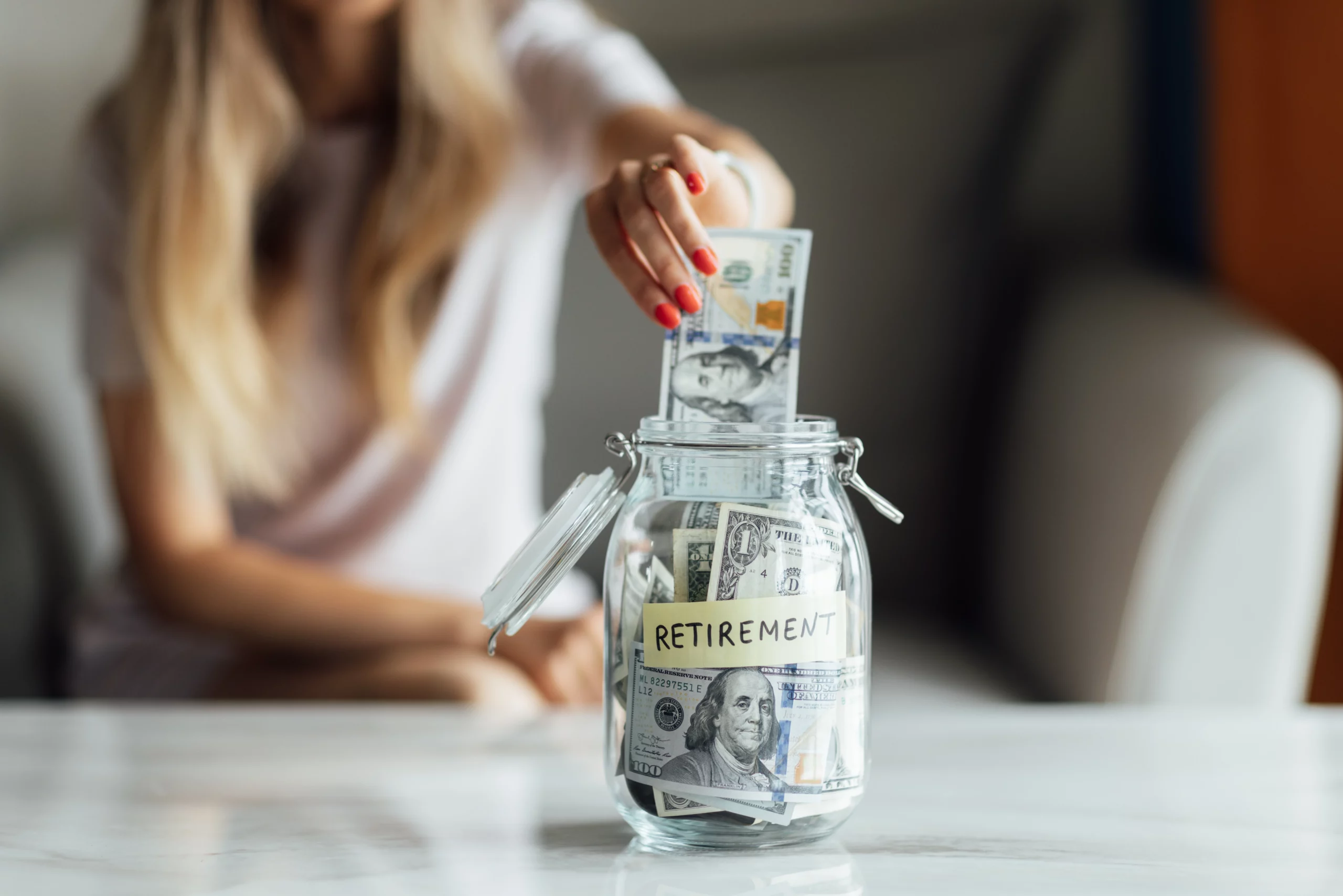 Person placing $100 bill into a cash-filled jar labeled "Retirement," symbolizing protected savings during bankruptcy.