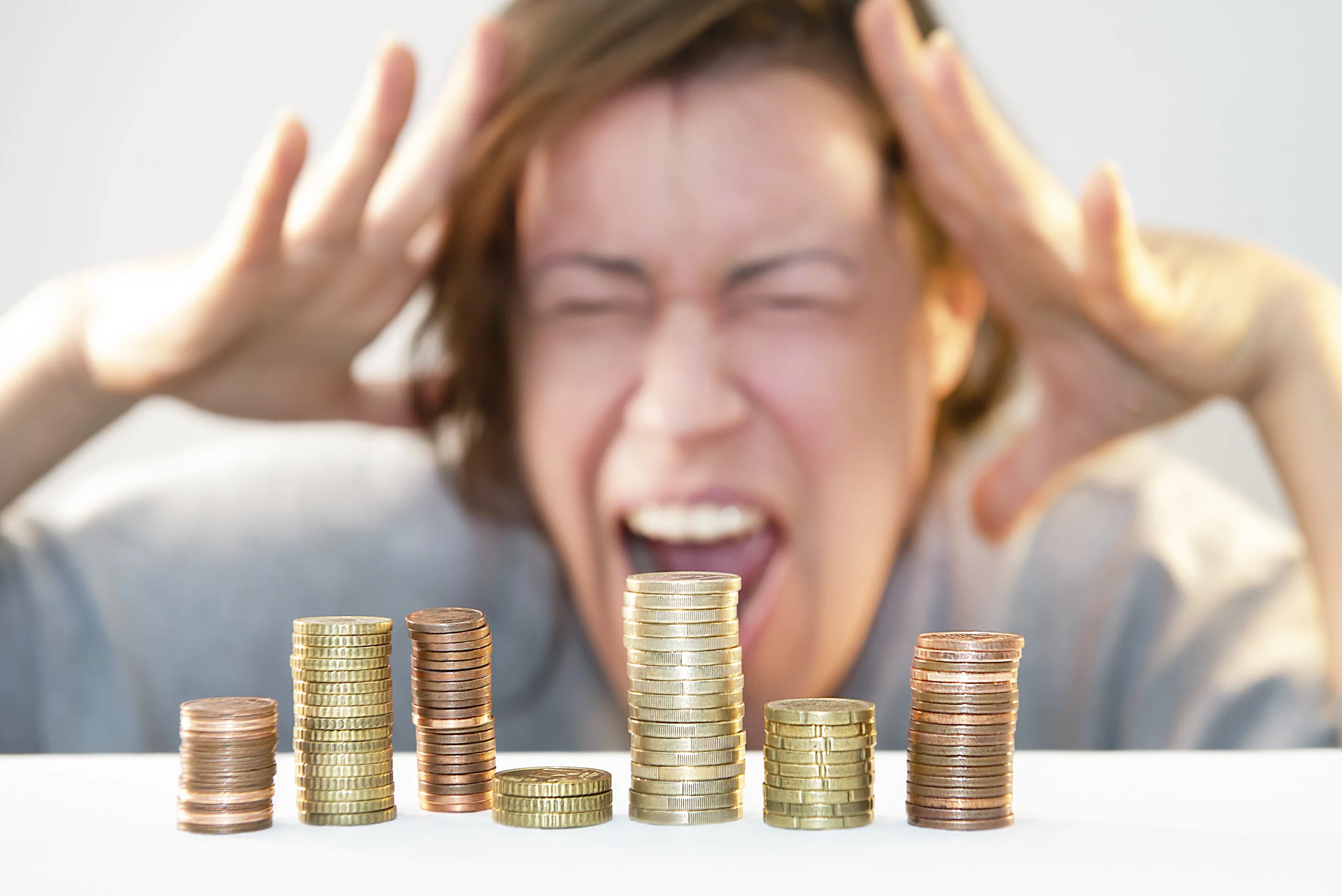 Stacks of coins at various heights in foreground, with a blurred individual in the background holding their head in stress—symbolizing financial distress from tax debt.