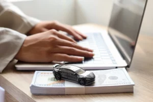 Toy car on hundred-dollar bills beside laptop, symbolizing missed car payments and risk of repossession in Oregon