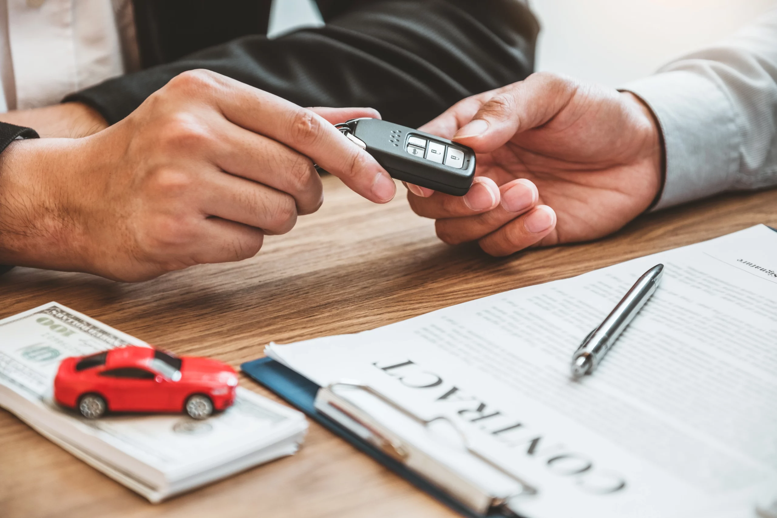 Hands exchanging car keys over a contract with cash and a toy car, symbolizing a car loan in Chapter 13 bankruptcy.