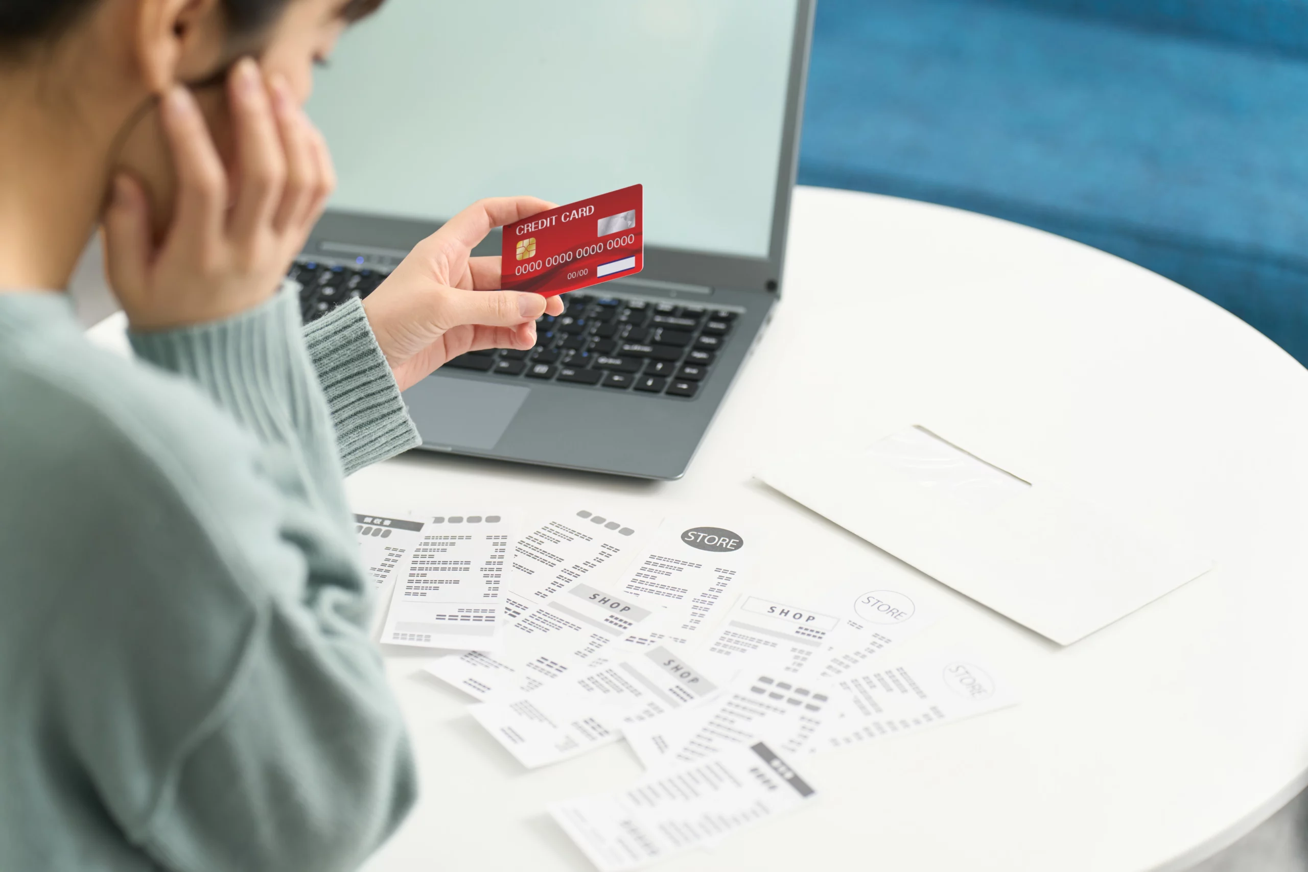 Woman holding a credit card while looking at a laptop screen, surrounded by multiple receipts on a table — illustrating financial concern, credit card debt, and the decision between Chapter 7 and Chapter 13 bankruptcy.