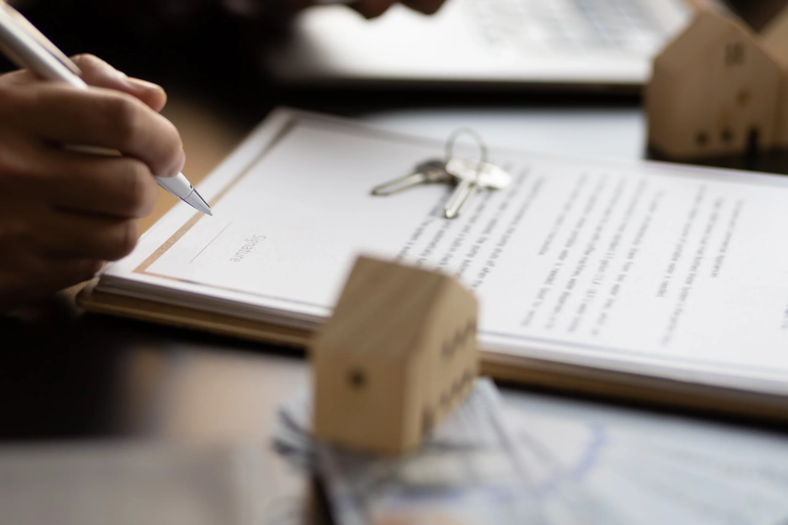Hand signing a legal document beside house figures and keys, illustrating how Chapter 7 bankruptcy affects mortgages and homeownership in Oregon.